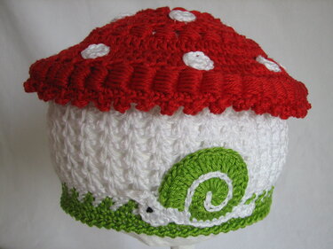 Gehäkelte Kinder‑Mütze in Pilzform mit rotem Hut, weißen Punkten und grüner Schnecke