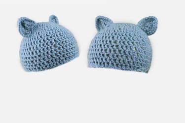 Zwei hellblaue gehäkelte Babymützen mit Ohren auf weißem Hintergrund