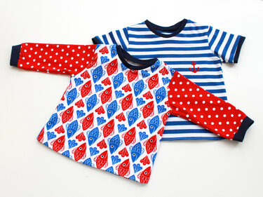 Zwei Kinder-Shirts: eines mit rot-blauem Fischmuster und gepunkteten Ärmeln, das andere blau-weiß gestreift mit kleinem roten Anker