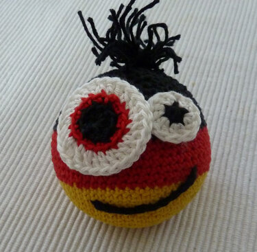 Gehäkelte Amigurumi-Kugel mit zwei großen Augen, schwarzer Quaste und gesticktem Mund