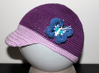 Gehäkelte Babymütze in Violett mit helllila Krempe und blauer Blüte auf Mannequinkopf