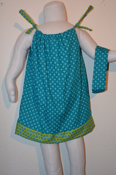 Türkises Trägerkleid mit geometrischem Muster und limettengrünen Bindebändern auf einer Schaufensterpuppe