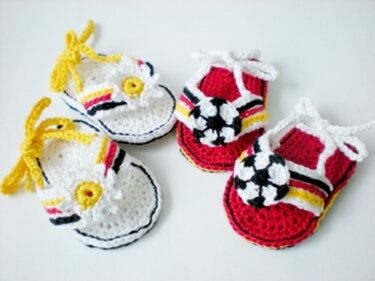 Zwei Paare gehäkelter Babyschuhe: weiß mit gelbem Kreis und farbigen Bändern; rot mit gehäkeltem Fußball und farbigen Bändern.