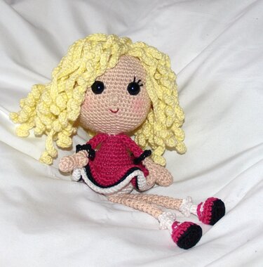 Gehäkelte Amigurumi-Puppe mit gelben Locken, pinkem Kleid und schwarzen Augen auf weißem Hintergrund