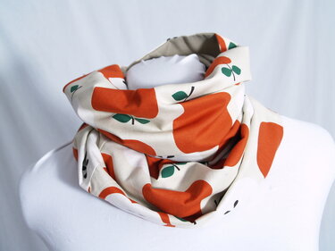 Genähter Schlauchschal aus gemustertem Stoff mit orangefarbenen Äpfeln, auf einer Schneiderpuppe präsentiert