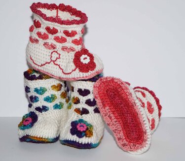 Gehäkelte weiße Babyschuhe mit Herz- und Blumenmustern in Rot, Pink und bunten Farben