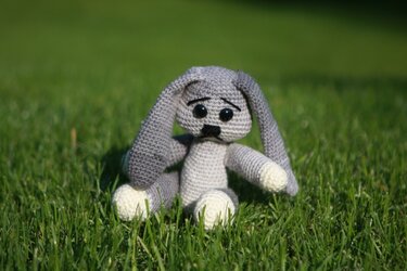 Gehäkelter grauer Amigurumi-Hase mit langen Ohren sitzt im Gras