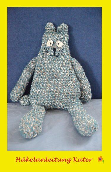 Gehäkelter Kater aus blau-grau meliertem Garn mit gesticktem Gesicht vor dunklem Hintergrund