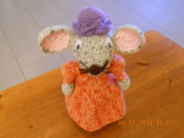Gehäkelte graue Amigurumi‑Maus mit rosa Ohren, orangefarbenem Kleid und lila Hut.