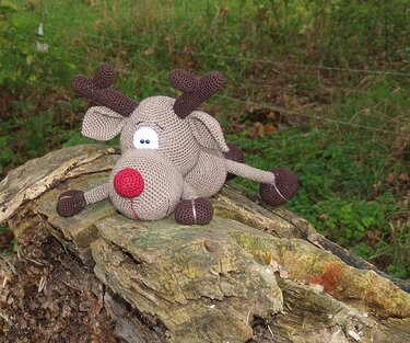 Nahaufnahme eines gehäkelten Amigurumi-Rentiers mit roter Nase und braunen Hufen
