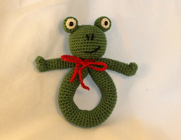 Gehäkelter grüner Frosch-Greifring mit roter Schleife, frontale Ansicht