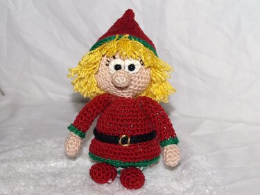 Gehäkelter roter Weihnachtswichtel mit gelbem Fransenhaar, schwarzem Gürtel und spitzer Mütze auf weißem Untergrund