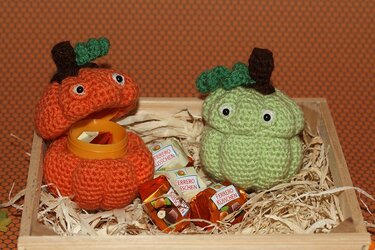 Zwei gehäkelte Kürbis-Amigurumi in einer Holzkiste, einer geöffnet mit Süßigkeiten im Inneren