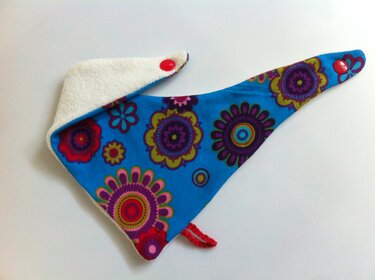 Verstellbares Baby-Halstuch blau mit buntem Blumenmuster, weißem Frottee-Innenfutter, zwei roten Druckknöpfen und kleiner roter Schlaufe, ausgelegt