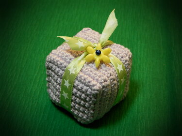 zarte gehäkelte Geschenkbox mit grünem Band und gelber Blumenapplikation auf grünem Hintergrund