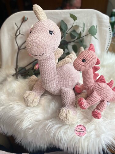 Zwei gehäkelte Amigurumi-Drachen in hell- und dunkelrosa auf flauschigem Untergrund