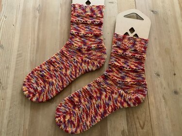Handgestrickte mehrfarbige Socken in Rot, Gelb und Lila auf Holz mit Kartoneinlagen