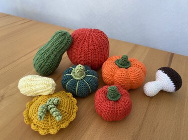 Gehäkelte Kürbisse in mehreren Farben mit Gurke, Maiskolben und Pilz auf einem Holztisch