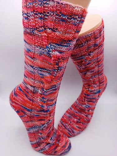 Mehrfarbige handgestrickte Socken mit Zopfmuster in Rot- und Blautönen vor hellem Hintergrund.