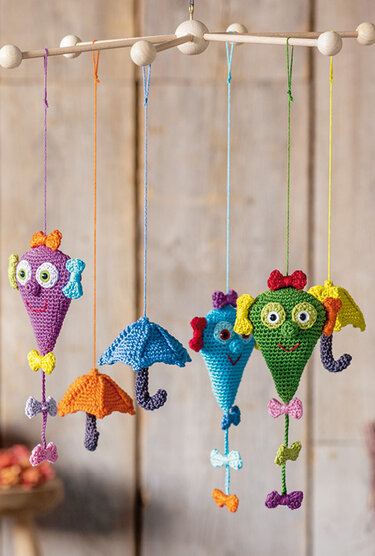 Mehrere gehäkelte bunte Drachen-Anhänger und kleine Schirme, an einem Holzgestell hängend