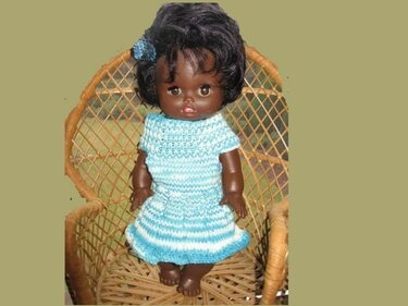 Kurzärmeliges gestricktes Puppenkleid in Türkis-Weiß mit Rüschensaum an einer Puppe im Rattanstuhl