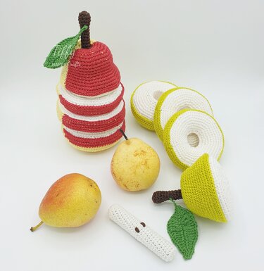 Crocheted pear stacking toy with removable green slices and a core piece, displayed next to two fresh pears on a white background.