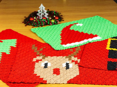 Drei gehäkelte Weihnachtsdeckchen mit Rentier-, Weihnachtsmannmützen- und Gürtelmotiven auf einem Holztisch.