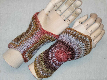 Paar gehäkelter fingerloser Damen-Handstulpen in braun-oliv-rosa Farbverlauf auf Holzhandmodellen