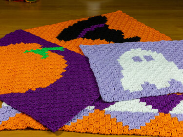 Drei handgehäkelte C2C-Quadrate mit Kürbis, Geist und Hexenhut auf lila und orangen Flächen