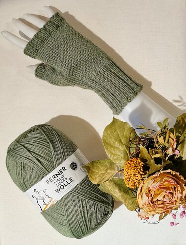 Olivgrüne gestrickte fingerlose Armstulpe auf Schaufensterhand mit Garn und Trockenblumen