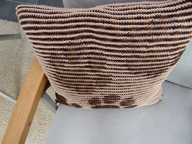 Gestrickter Kissenbezug in Beige und Braun mit Streifenmuster auf einem Stuhl