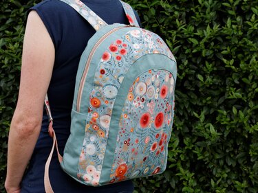 Türkisfarbener Alltagsrucksack mit floralen Einsätzen und Reißverschluss, auf dem Rücken getragen