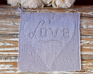 Gestricktes quadratisches Tuch in lila mit Herz- und LOVE-Muster auf Holzuntergrund.