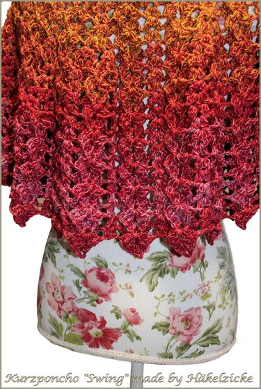 Gehäkelter Kurzponcho rot
‑orange‑braun mit Loch- und Spitzenmuster auf Schneiderpuppe