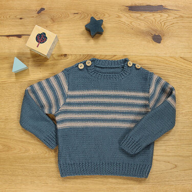 Blau-beiger gestreifter gestrickter Kinderpullover mit drei Schulterknöpfen auf Holzhintergrund
