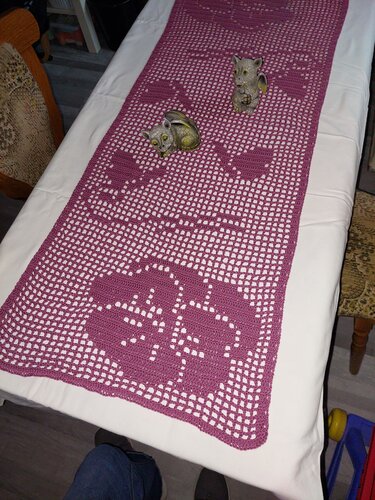 Lila gehäkelter Tischläufer mit wiederkehrendem Filethäkel-Blumenmuster auf weißer Tischdecke