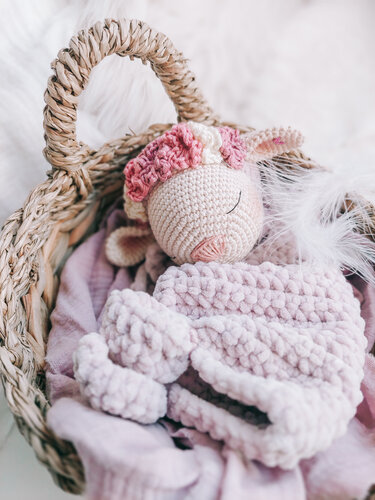 Crocheted pink lamb snuggle blanket with a floral headband in a woven basket with white feathers