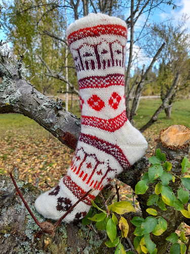 Handgestrickte cremefarbene Socke mit rot-braunem Haus- und Rautenmuster auf Ast