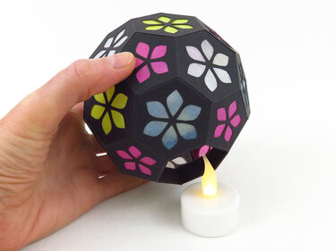 Hand hält Papierlaterne mit bunten Blumenfenstern über batteriebetriebenem Teelicht