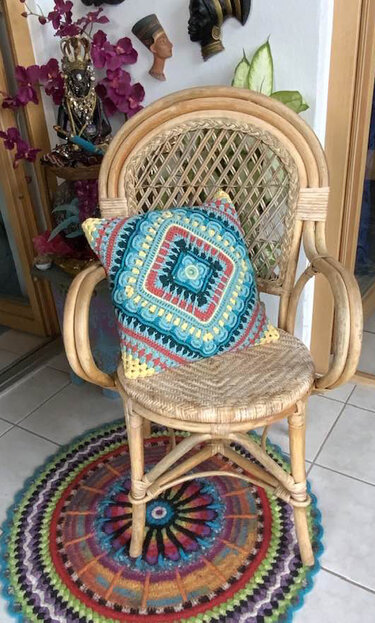 Boho-Arrangement mit buntem gehäkeltem Kissen auf Korbstuhl und rundem Häkelteppich