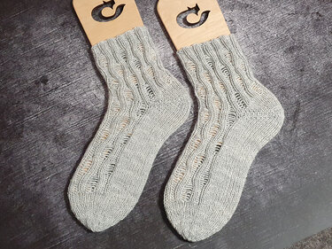 Paar hellgraue gestrickte Socken mit Ajour-Lochmuster auf Holzspannern auf dunkelgrauem Untergrund