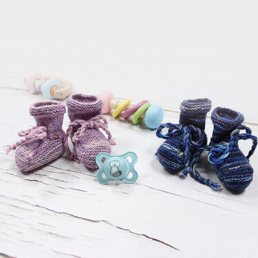 Zwei Paar einfache gestrickte Babyschuhe mit Bändchen, rosa/lila und blau, mit Schnuller und Holzspielzeug