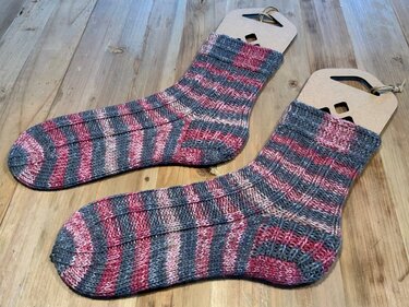 Gestricktes Paar Ringelsocken grau und rosa auf Holzsockenform liegend