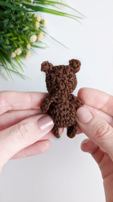 Small brown crocheted teddy bear held in hands, back view