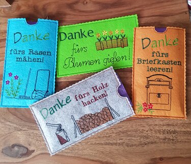 Vier bunte, bestickte Filzhüllen mit verschiedenen ‚Danke‘-Texten und kleinen Stickillustrationen von Werkzeugen und Blumen.