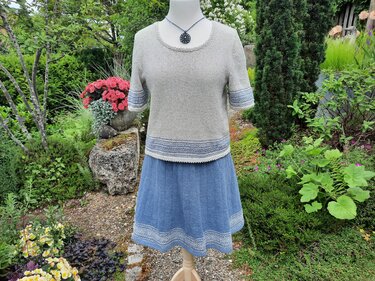 Schaufensterpuppe mit hellgrauem gestricktem Kurzarmtop und blauem ausgestelltem Rock im Garten