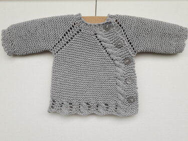Gestrickte graue Babyjacke mit diagonaler Knopfleiste, Zopfmuster und Lochsaum