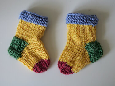 Gelbe Babysocken gestrickt mit blauem Bündchen, grüner Ferse und roter Spitze