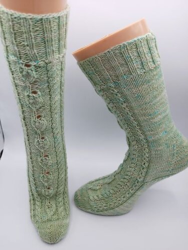 Zwei mintgrüne gestrickte Socken mit Zopf- und Lochmuster auf Sockenformen