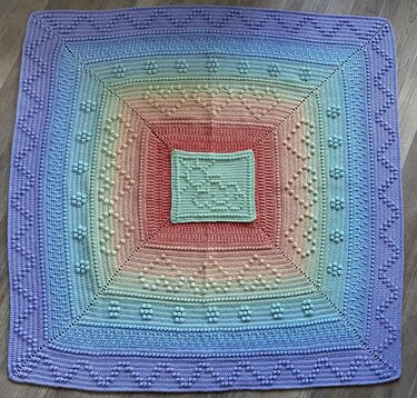 Quadratische gehäkelte Babydecke in pastelligen Regenbogenfarben mit erhabenen Bobbelmustern und gezacktem Rand, flach ausgelegt